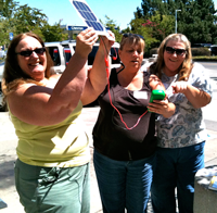 three people outdoors holding up circuit boards and smiling